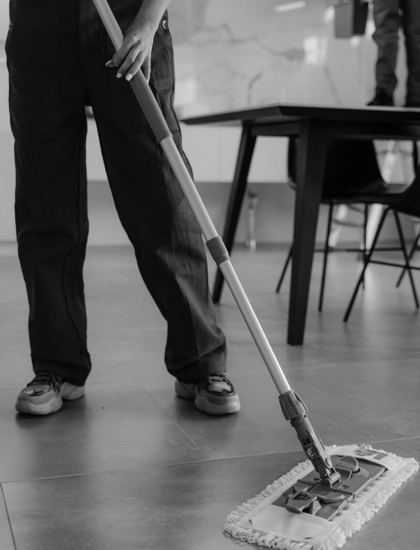 Cleaner flat-mopping a tiled floor beside a meeting table